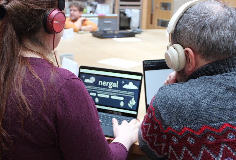 photo of two people looking at a laptop playing nergal, viewed from behind, they are both wearing headphones