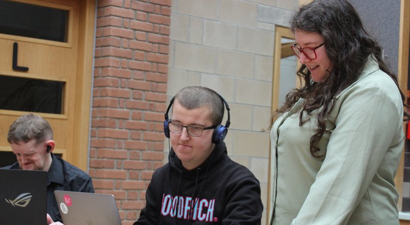 photo of 3 people, all are playing the game and two have headphones on, one is standing and all are smiling