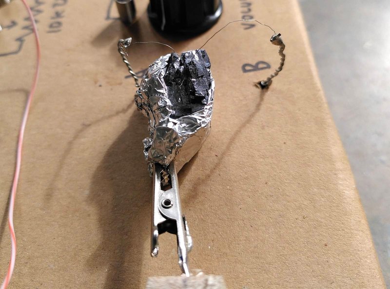 photo of galena crystal in foil with two thin wires touching it