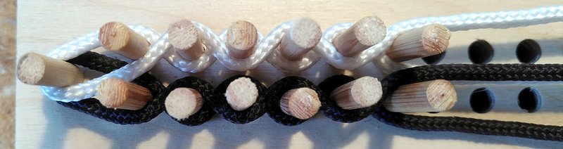 Two rows of wooden pegs with black and white threads woven between them