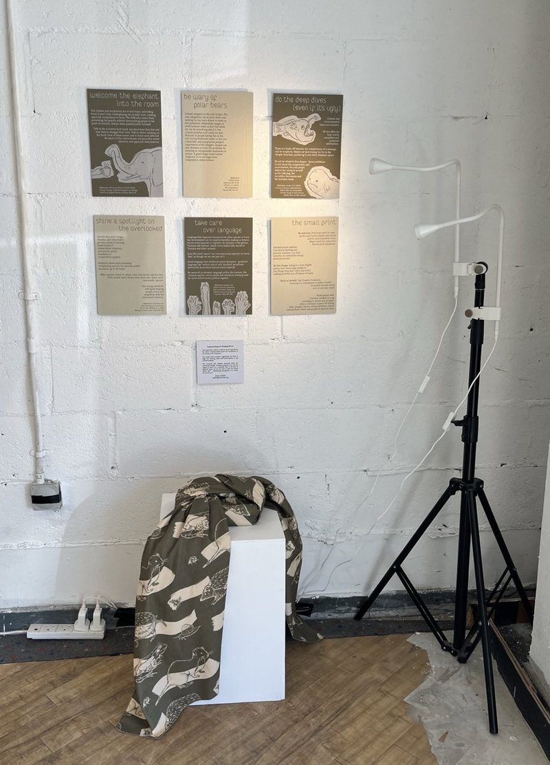 6 prints lit from the side, and a wrapped box on a plinth with fabric draping to the floor