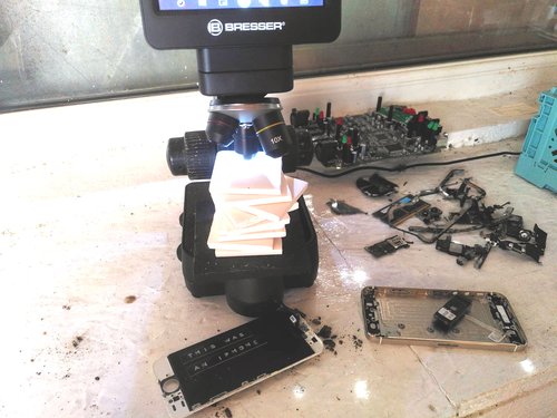 Microscope with a stack of streak plates used to raise rock samples into focus, surroundied by smashed iPhones and circuit boards.